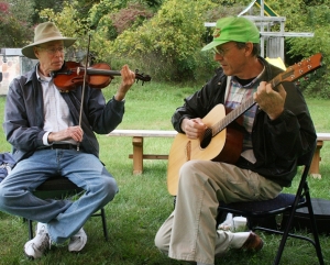 Two men play violin and guitar while sitting outdoors